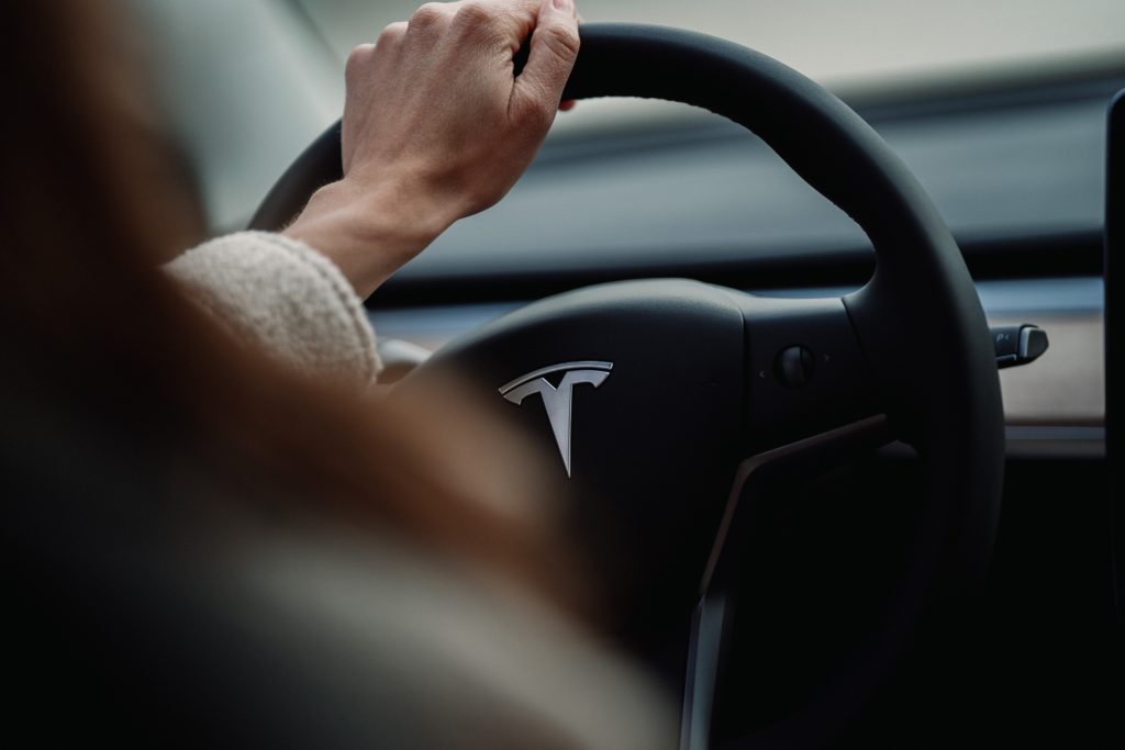 Woman driving a Tesla holding the steering wheel (Image: Jenny Ueberberg - Unsplash)